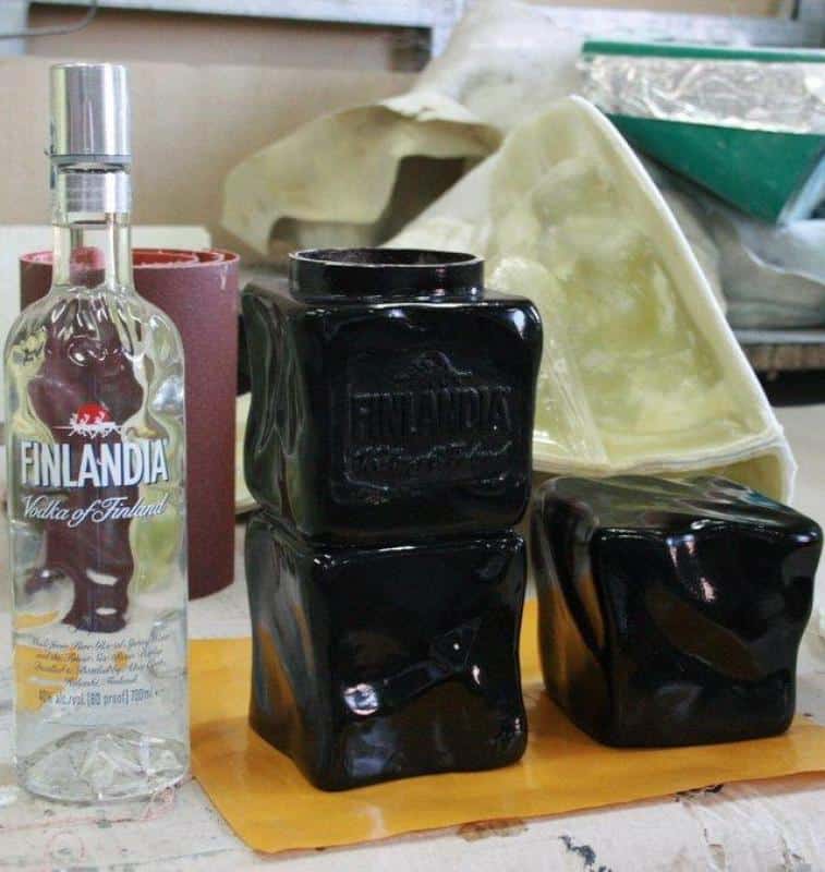 Promotional packaging Finlandia 2 Butelka Finlandia Vodka To/1750 ml oraz trzy czarne, zdeformowane butelki Finlandia umieszczone na stole roboczym.