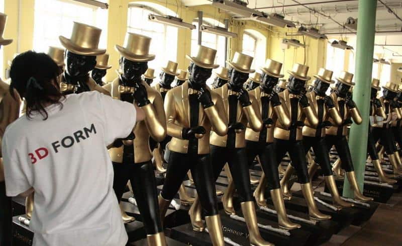 Rzędy manekinów ubrane we złote garnitury i cylindry, osoba w białej koszulce z napisem 