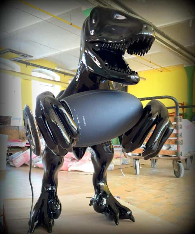 Rzeźba błyszczącego czarnego dinozaura trzymającego duży głośnik w jasnym pomieszczeniu.