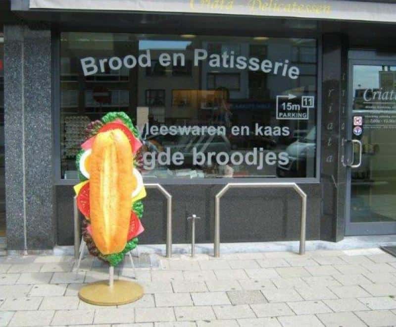 oryg_064490685_1129949550544944_1465385417682452480_o Front of a bakery with a window advertisement and a large sandwich board outside.