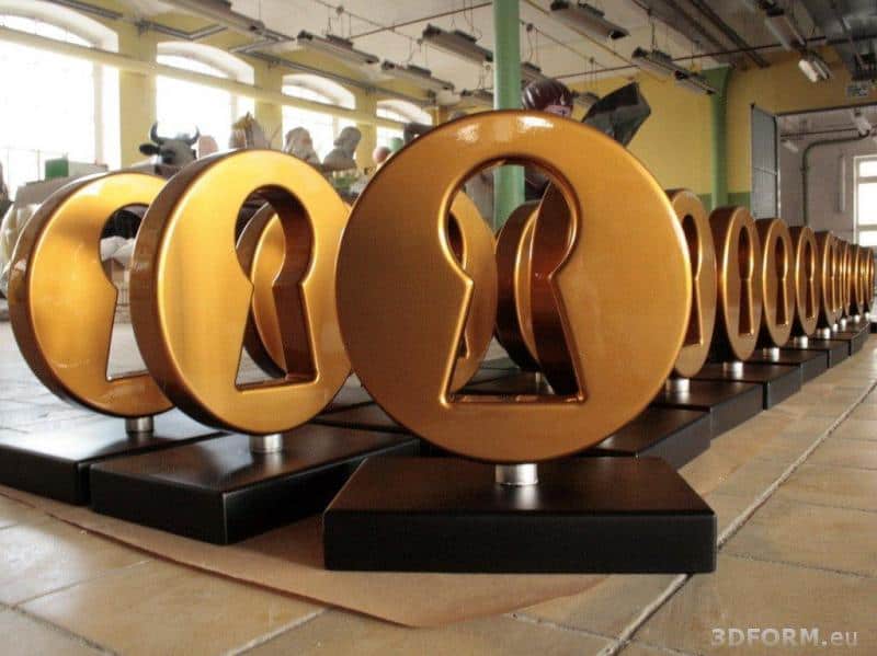 oryg_064490685_1129949550544944_1465385417682452480_o Golden keyhole-shaped trophies on black bases lined up on a workshop floor.