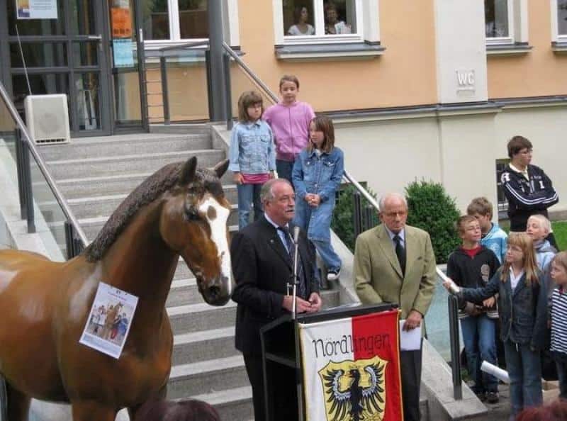 Event Horse Figures 2 Grupa osób podczas ceremonii na zewnątrz, przy posągu konia i mównicy z herbem
