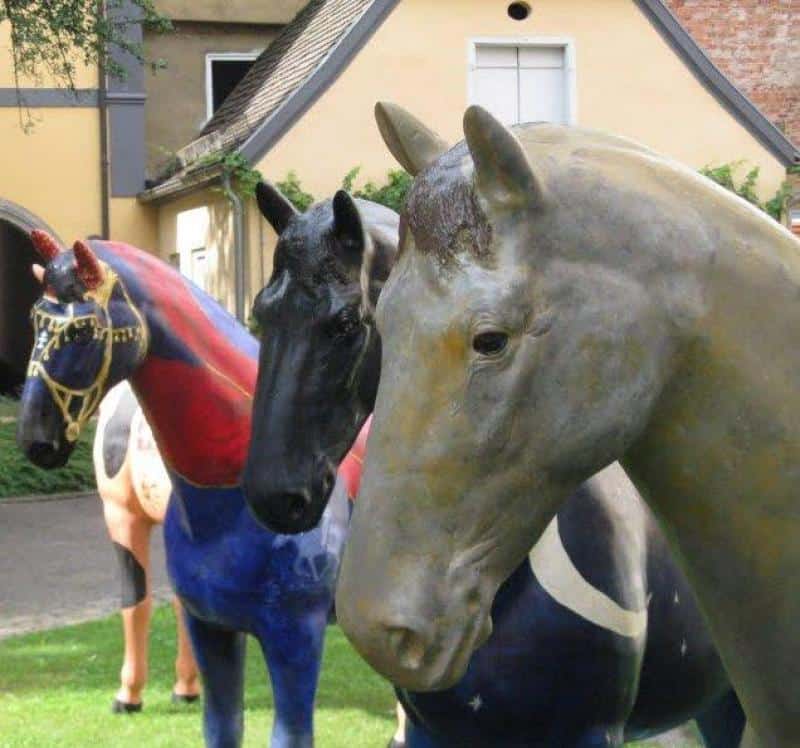 Event Horse Figures 4 Trzy kolorowe rzeźby koni ustawione w ogrodzie przed domem.