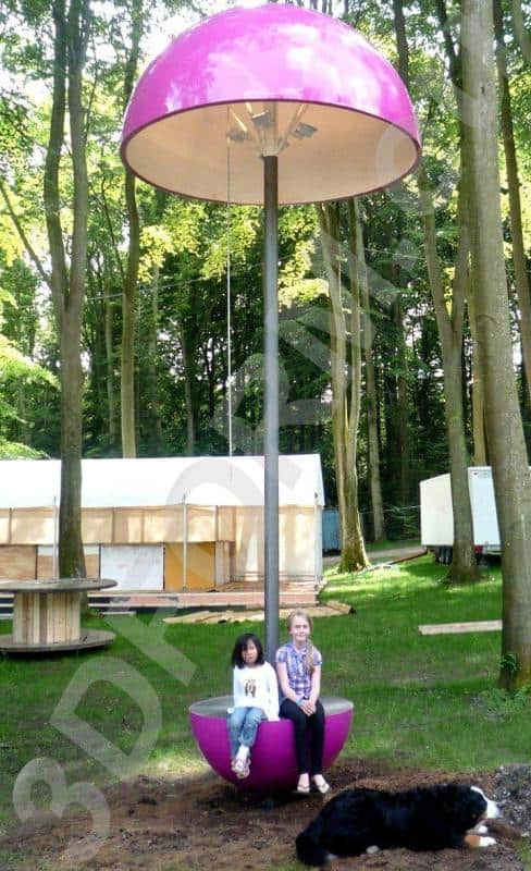 Festival Lamps 2 Dwoje dzieci siedzących na różowej huśtawce w kształcie grzyba w lesie, obok leży czarny pies.