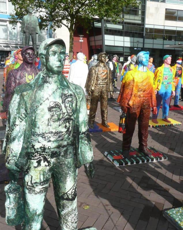 Colorful statues of miners standing on a pavement near modern buildings and trees.