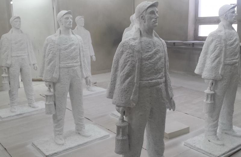 Posągi górników trzymających lampy górnicze ustawione w pomieszczeniu.