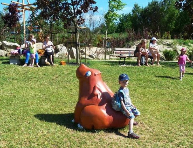 Dragons in the amusement park 3 Chłopiec siedzący na rzeźbie zwierzęcia w parku, w tle kilka osób i drzewa.