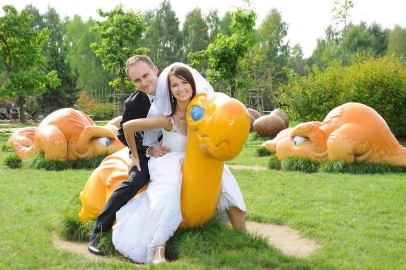 Dragons in the amusement park 2 Para młoda siedząca na dużej, pomarańczowej figurce zwierzęcia w parku.