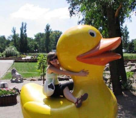Figures in a theme park 3 Osoba obejmująca dużą plastikową żółtą kaczkę w parku.