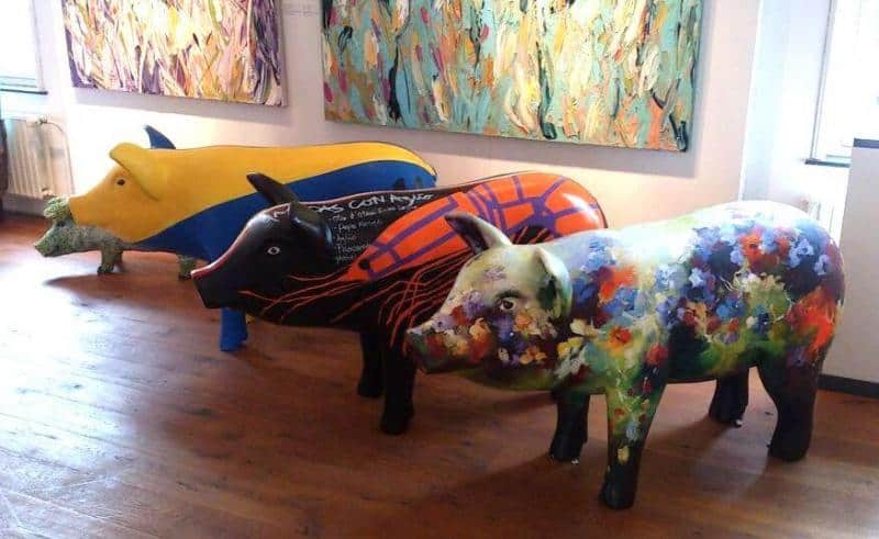 Artistically painted animal figures 1 Trzy kolorowe rzeźby świni w galerii sztuki, każda ozdobiona różnorodnymi wzorami i malowidłami.