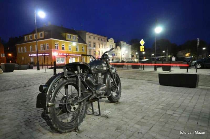 Iconic Motorcycle - Monument in Żagań 4 Motocykl na placu miejskim nocą, w tle oświetlone kamienice.