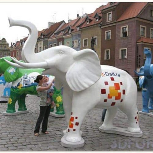 Colorful elephant statues in a public square with a person interacting with one of the statues, and buildings in the background.