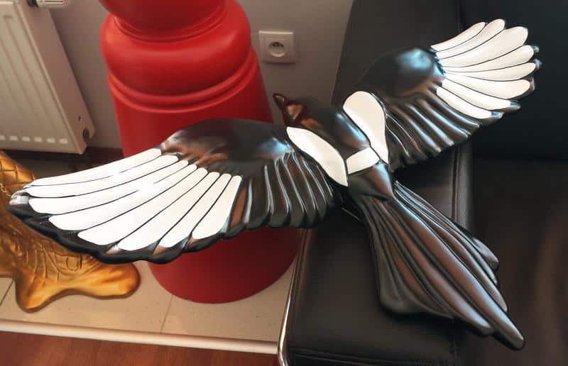 Flock of Magpies in Berlin 3 Czarna rzeźba ptaka z rozłożonymi skrzydłami leżąca na kanapie.