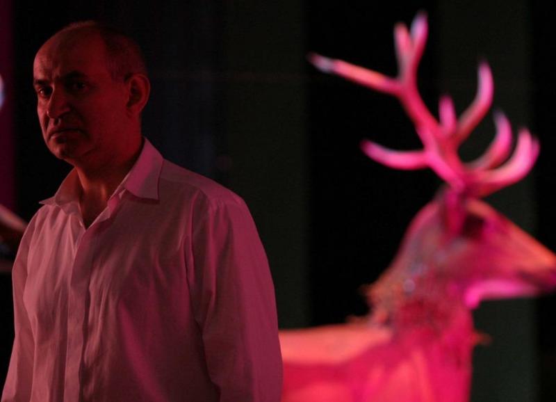 Stage design elements for the Dramatic Theatre of the Capital City of Warsaw 2 Mężczyzna w białej koszuli stojący obok różowo podświetlonego jelenia.