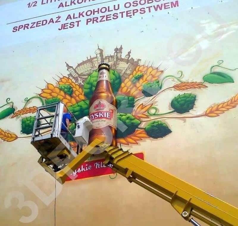 Three-dimensional mural TYSKIE 2 Osoba na podnośniku malująca reklamę piwa Tyskie na ścianie budynku.