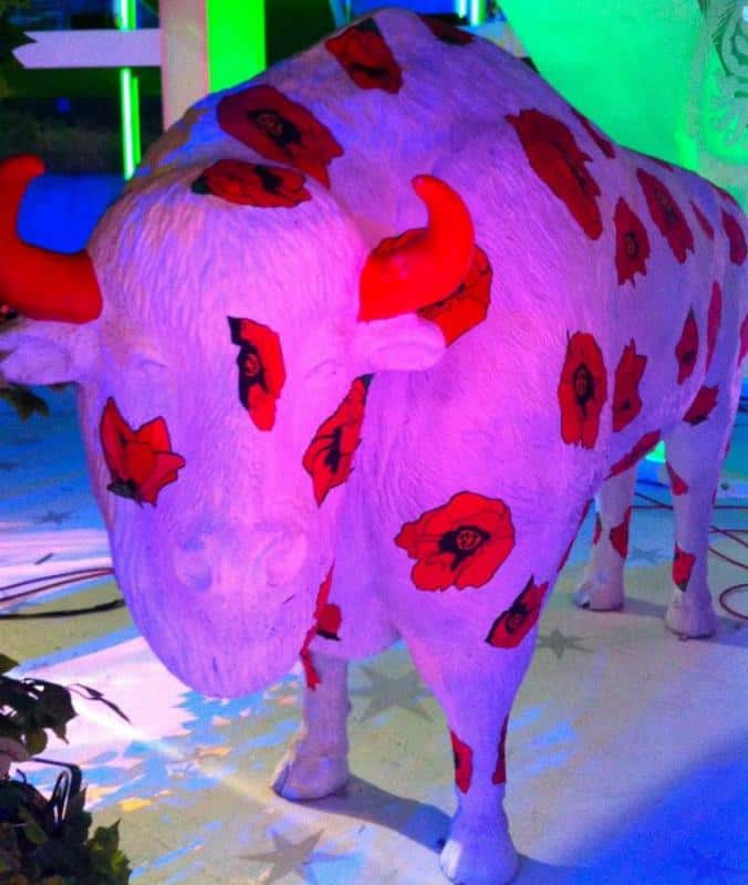 Bisons in Rzeźba byka pomalowana na biało, z czerwonymi makami i czerwonymi rogami.