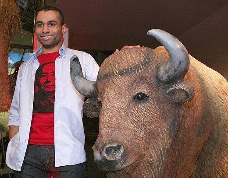 Bisons in Mężczyzna stojący obok rzeźby żubra, trzymający rękę na jego grzbiecie.