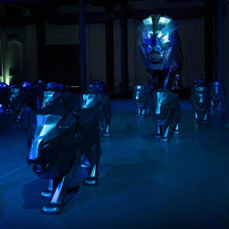 Peugeot lion fiberglass advertising sculpture 1 Metalowe rzeźby lwów w ciemnym, niebiesko oświetlonym pomieszczeniu.