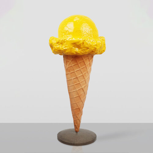 Sculpture of a yellow ice cream scoop on a waffle cone mounted on a round gray base against a plain light background.