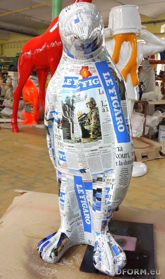 Large Fiberglass Penguin Statue - Natural Colors. 3 Statue of a penguin covered in newspaper clippings, standing indoors surrounded by other colorful animal sculptures.