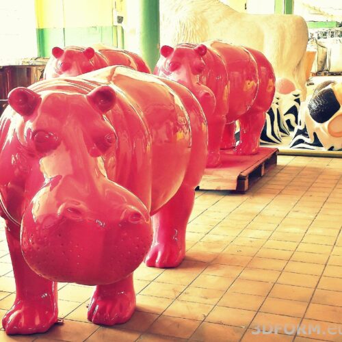 Bright pink hippo statues in an indoor space with other large animal sculptures in the background.