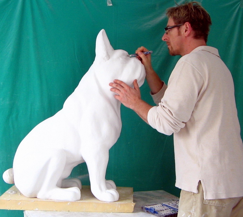 Middle size seated bulldog 2 Artist working on a large white dog sculpture against a green background.