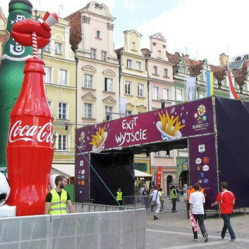 Large inflatable Coca-Cola and Heineken bottles flank a sign reading
