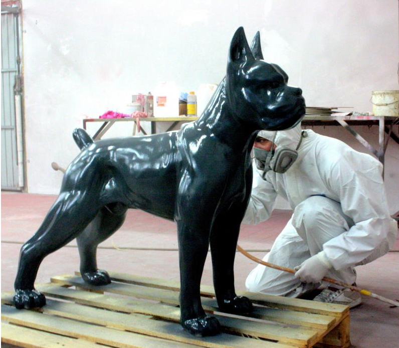 Boxer Dog Figure Standing - Single Color 1 A person wearing a protective suit and mask is spray-painting a large, shiny black statue of a dog standing on a wooden pallet.
