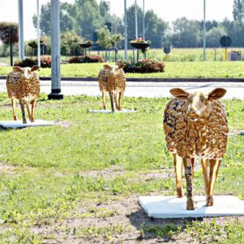 Golden sheep sculptures on grassy area with trees and bushes in the background.