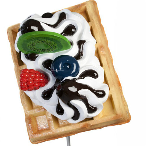 A waffle topped with whipped cream, chocolate syrup, kiwi slice, blueberries, and raspberries.