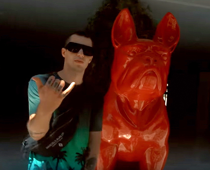 Giant sitting bulldog statue, single-colored. 6 A man wearing sunglasses and a green shirt stands next to a large red statue of a dog.