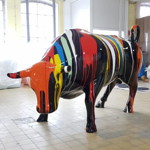 Colorful bull sculpture with vibrant paint drips in multiple hues standing on a tiled floor indoors.