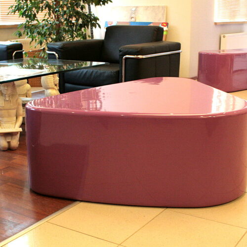 Modern living room with black chairs, a glass coffee table, pink glossy triangular bench, and an Egyptian statue.
