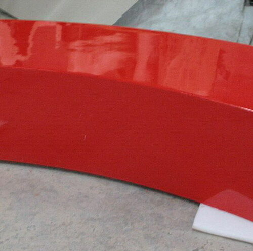 A red, curved, rectangular bench with a smooth, shiny surface, supported by white blocks underneath.