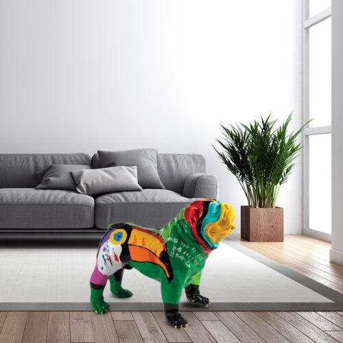A living room with a grey sofa, white cushions, a potted plant in a wooden planter, and a colorful dog sculpture on the floor.