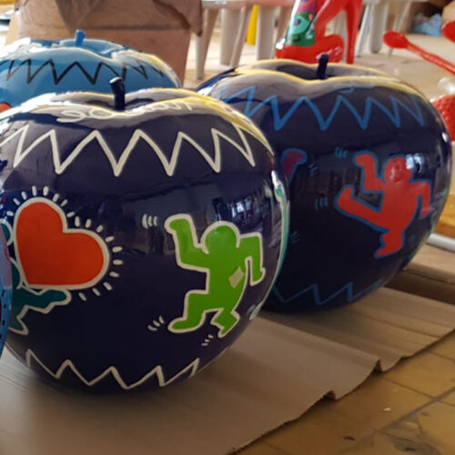 Blue apples with colorful, abstract figures and heart designs in the style of Keith Haring on them.