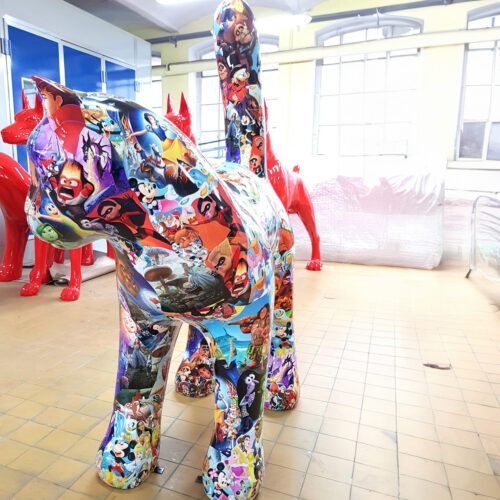 A large cat sculpture covered in colorful images from various animated movies, with two red dog sculptures in the background.
