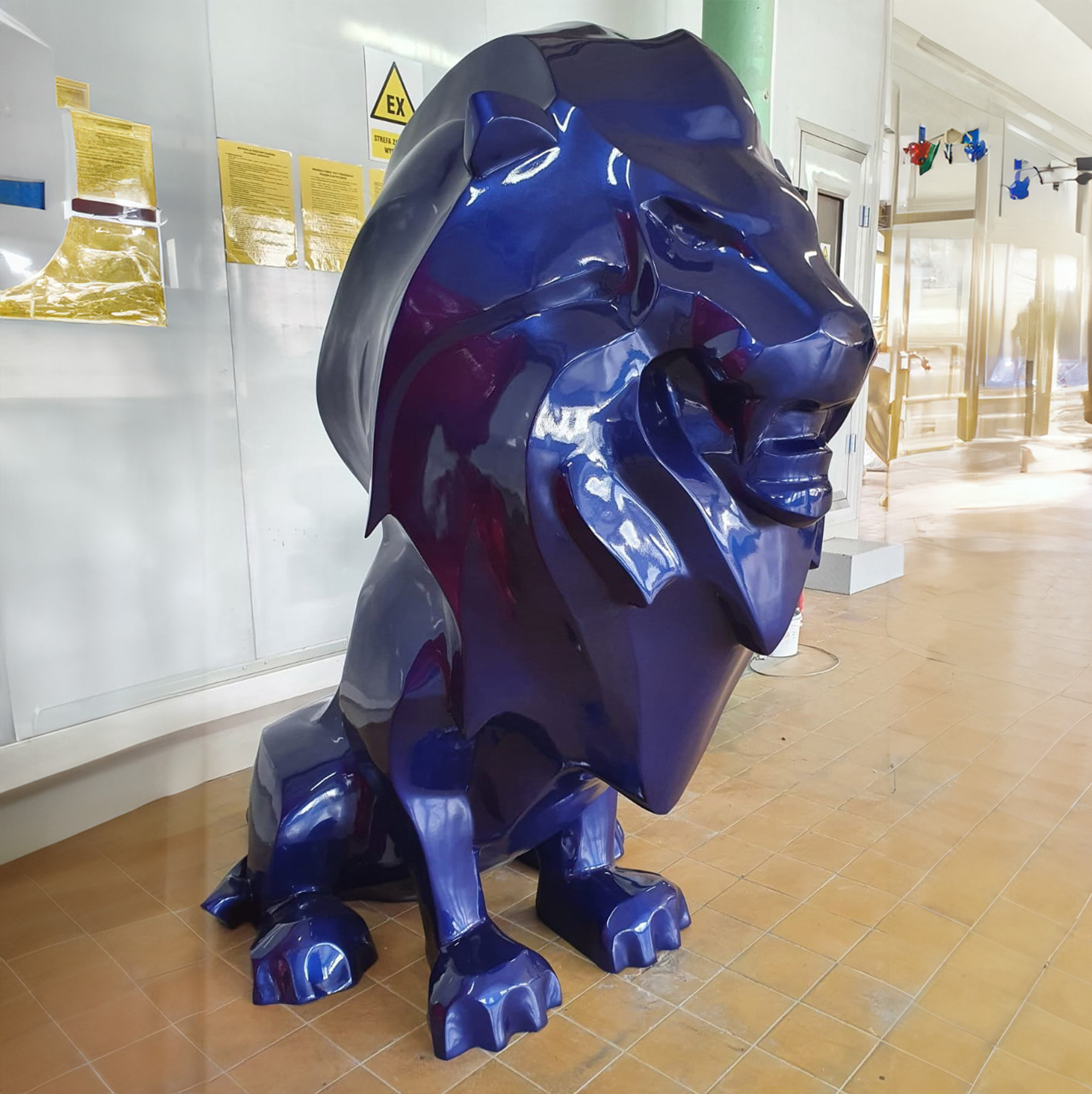 Large, glossy blue lion statue displayed indoors on a tiled floor.