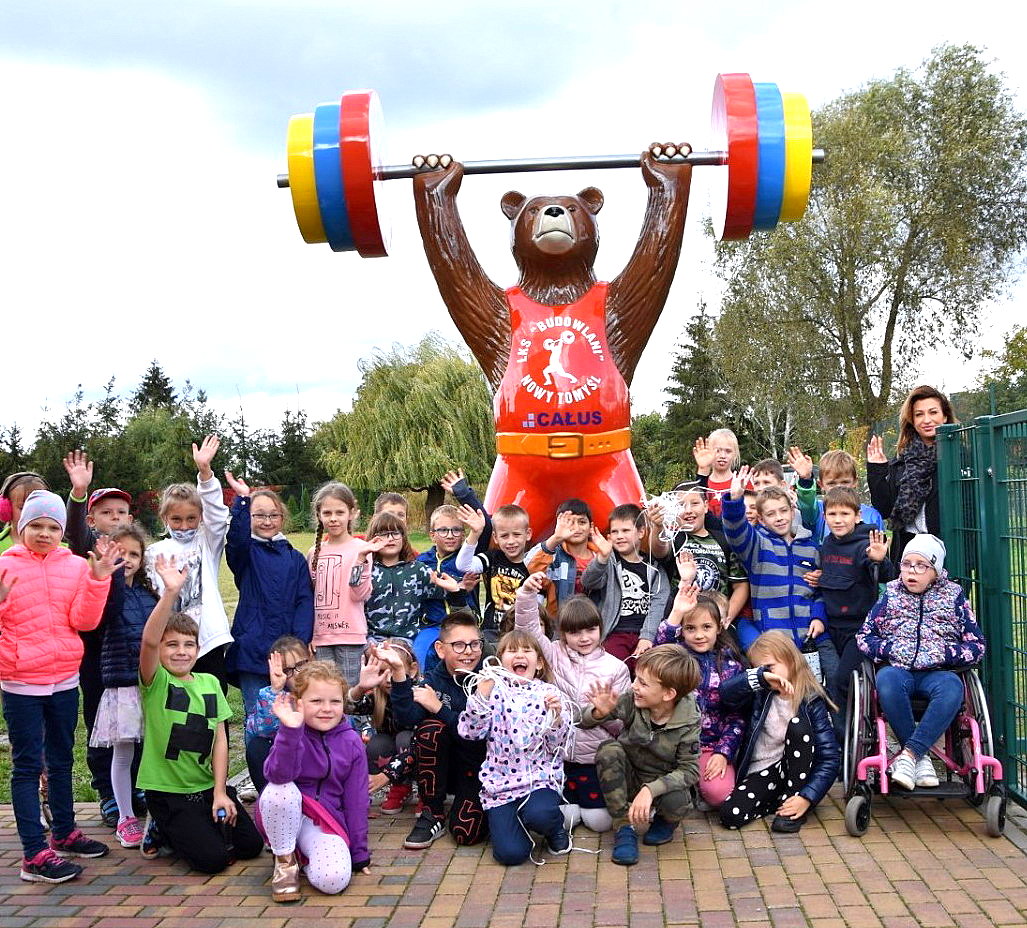 Group of children posing in front of a large bear statue holding a barbell.