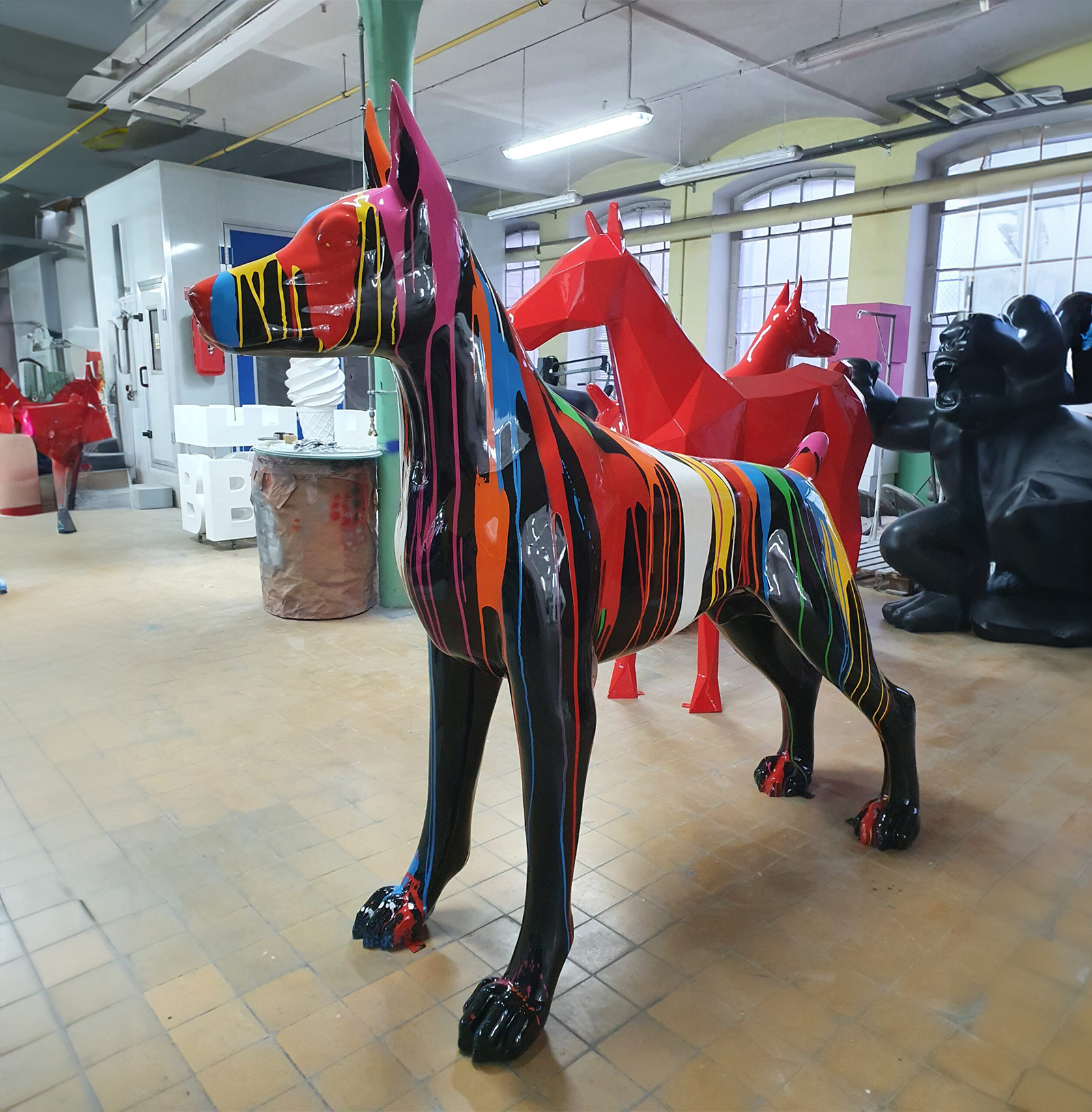 Large Doberman Colorful Fiberphglass Statue 2 Colorful, striped statue of a dog in an art studio with other animal statues in the background.