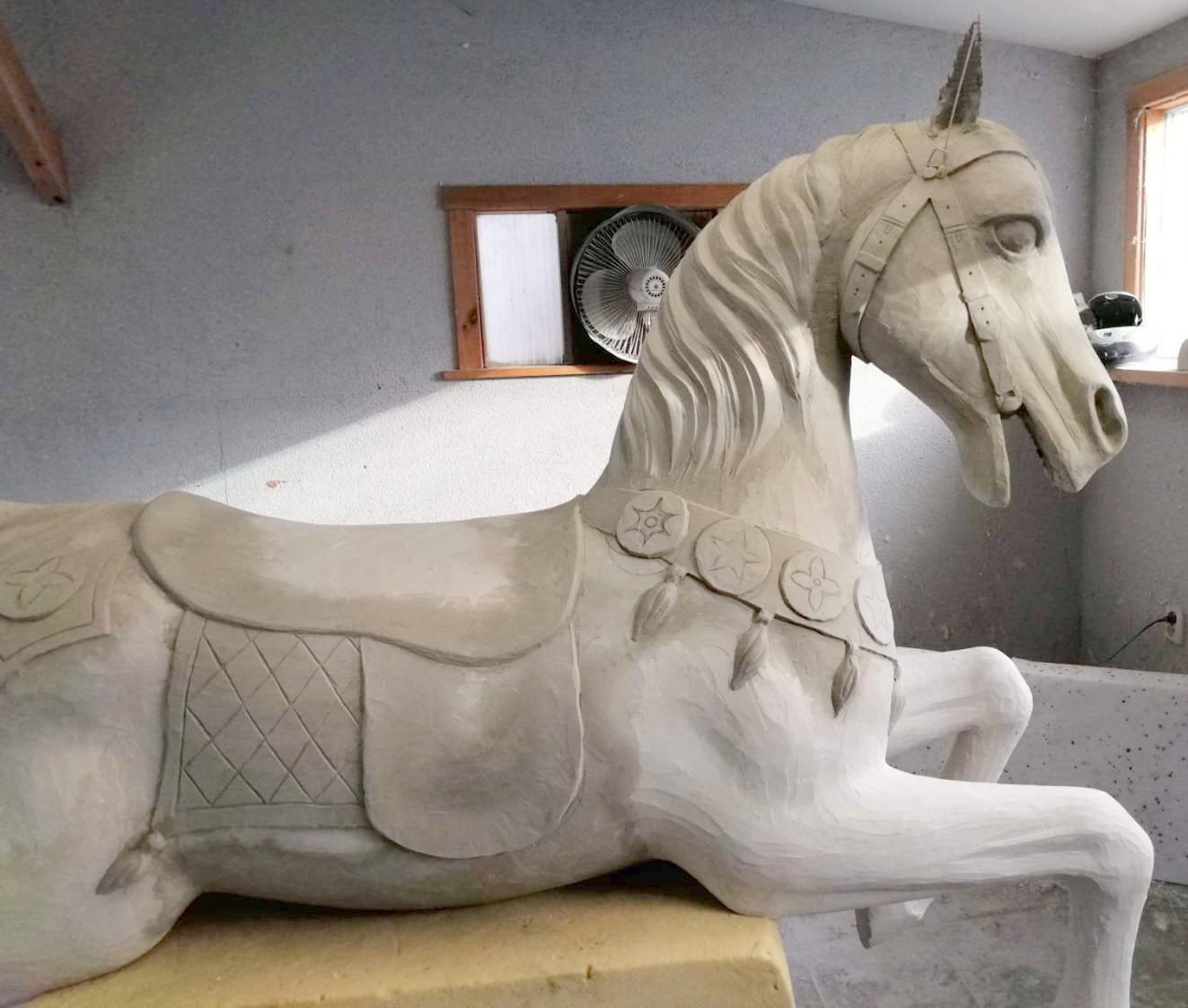 Carousel of unique unicorns 5 Koń rzeźbiony w drewnie z siodłem i ozdobami w pracowni.