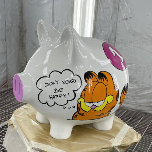 Large white piggy bank with painted pink nostrils and a cartoon character. The character has a speech bubble that reads, 
