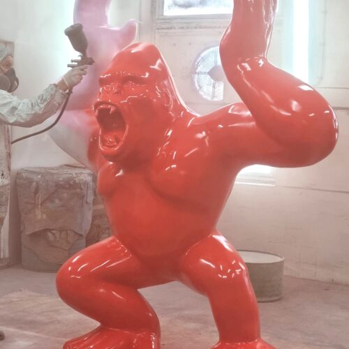 A worker spray-paints a large, red gorilla statue inside a workshop.