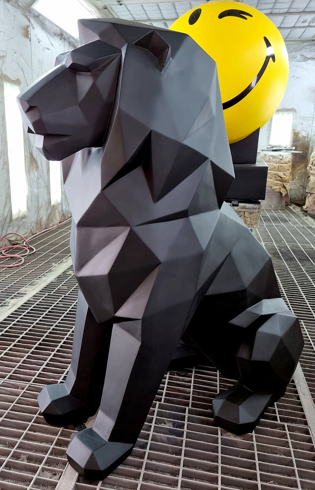 Monochromatic Geometric Lion Figure 3 Geometric black lion statue with a large emoji smiley face in an industrial setting.