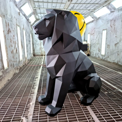 Black geometric lion sculpture in an industrial setting with a yellow smiley balloon in the background.