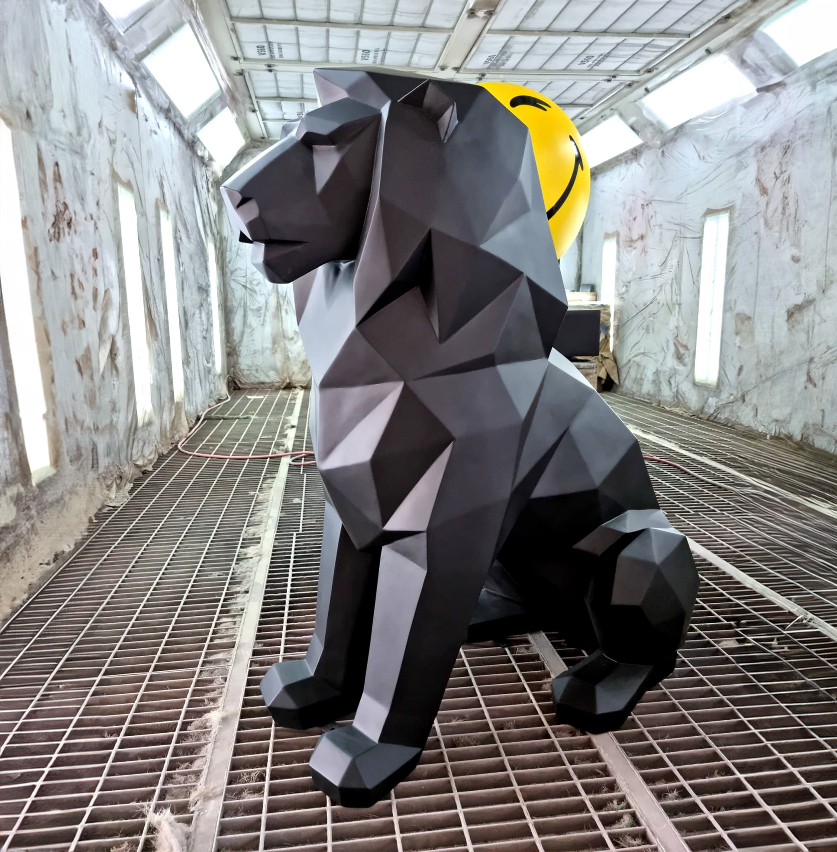 Geometric lion sculpture single color 1 Black geometric lion sculpture in an industrial setting with a yellow smiley balloon in the background.