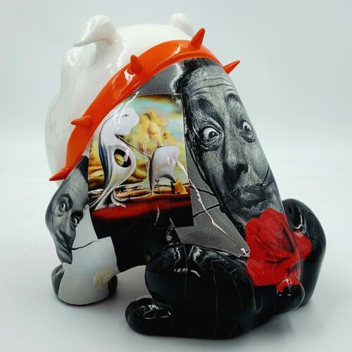 A stylized sculpture of a bulldog with a white body and black legs. It features a mixed-media collage with black-and-white photographic faces, colorful surrealist art, and an orange spiked collar.