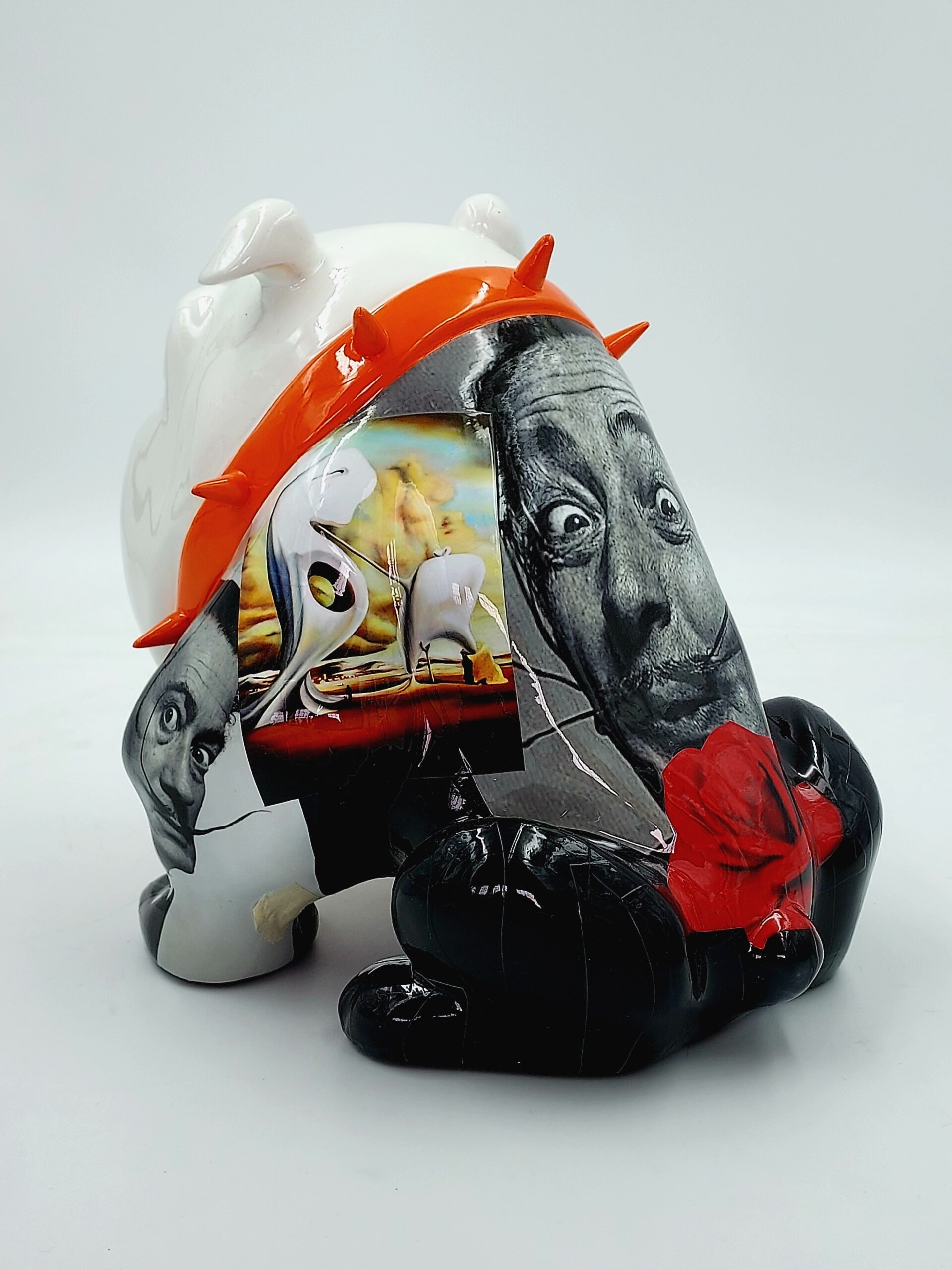 Bulldog Avella 55cm dog - Mustache 2 A stylized sculpture of a bulldog with a white body and black legs. It features a mixed-media collage with black-and-white photographic faces, colorful surrealist art, and an orange spiked collar.