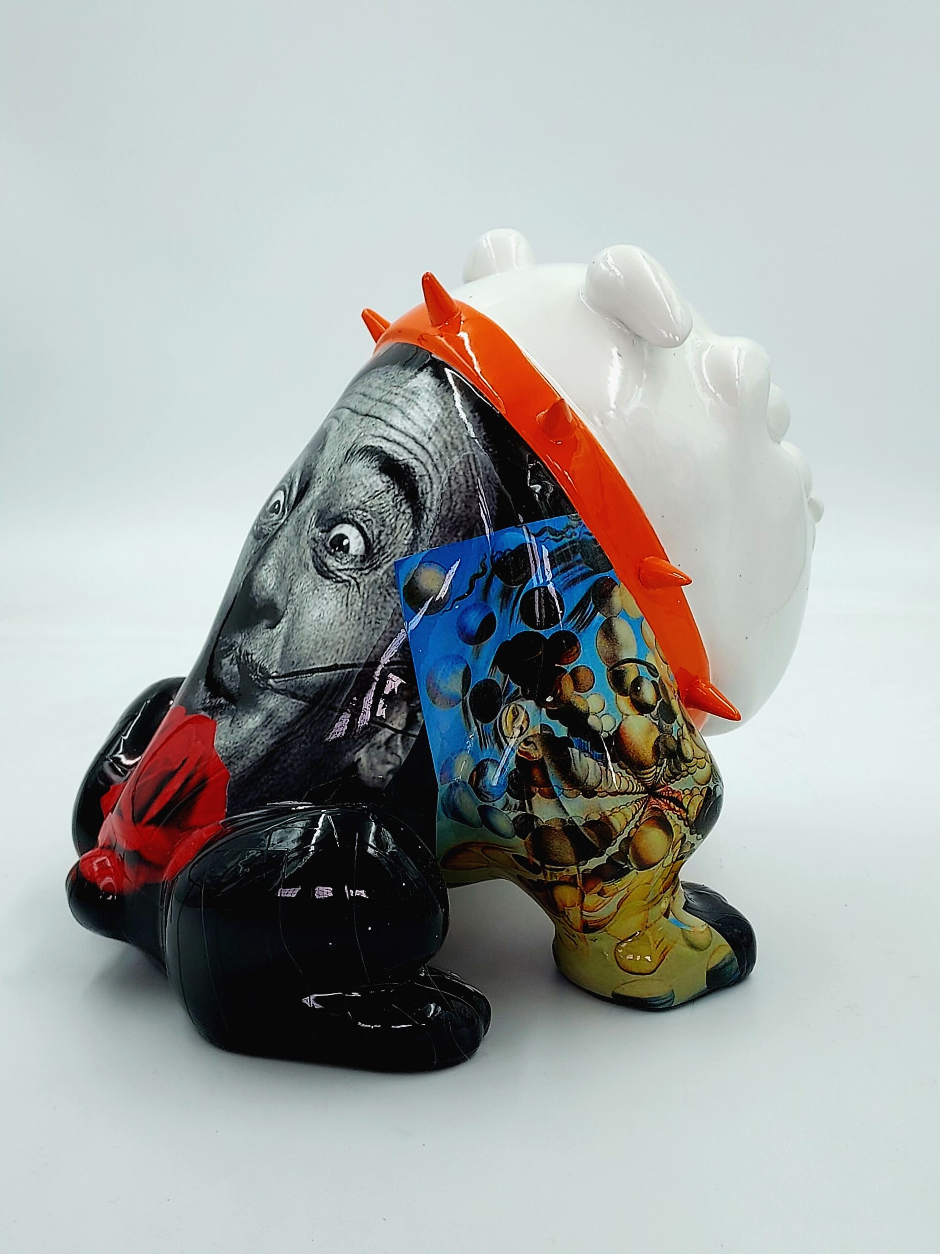 Bulldog Avella 55cm dog - Mustache 3 A colorful, abstract sculpture featuring a mix of black and white photographic imagery, vivid colors, and patterns. The sculpture has exaggerated facial features and is adorned with an orange spiked crown.