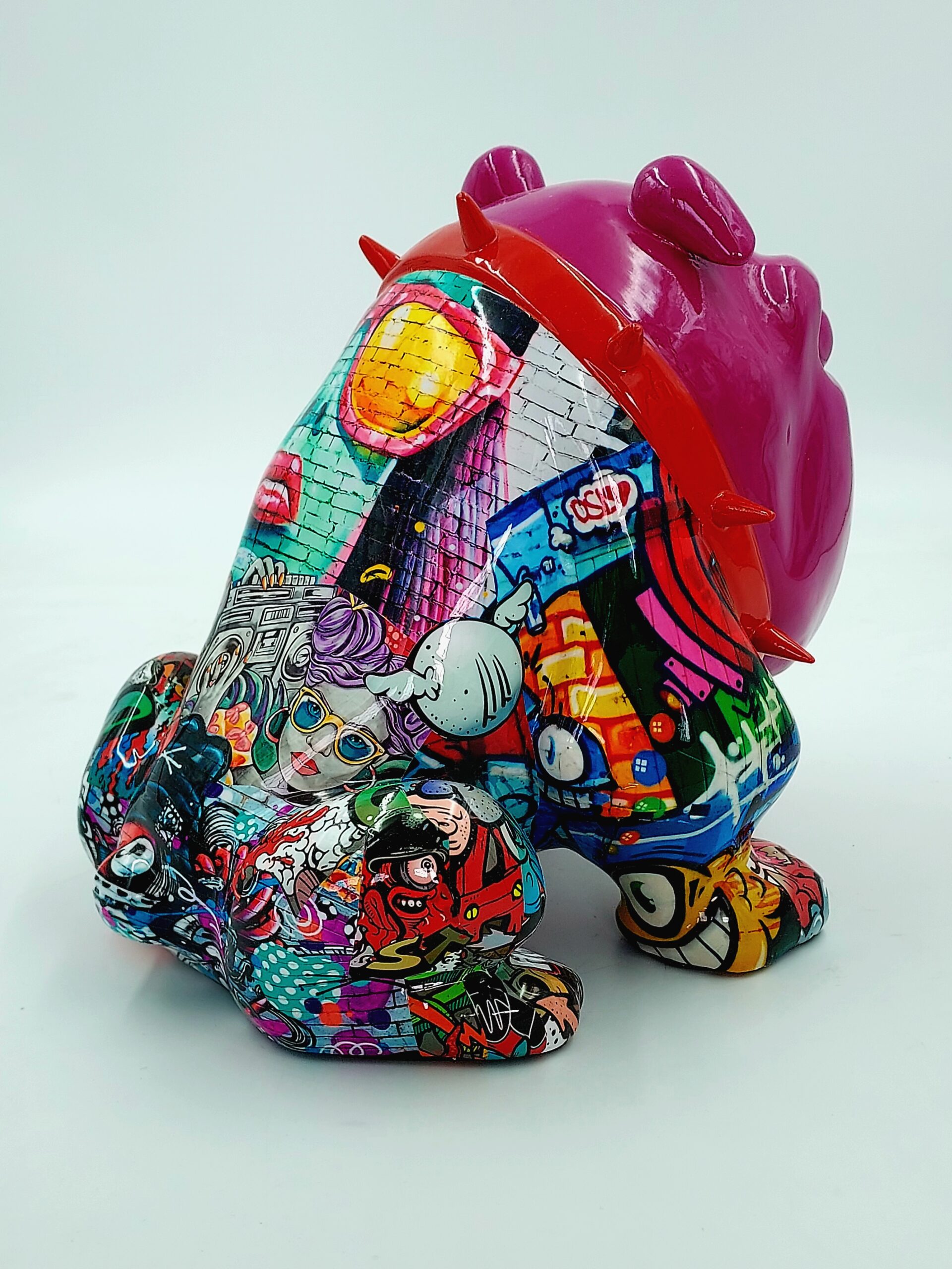 Bulldog Avella Dog 55cm - graffiti 3 A colorful, graffiti-styled sculpture of a sitting bulldog with a pink head and spiked red collar, adorned with various vibrant, pop-art-inspired designs and images.
